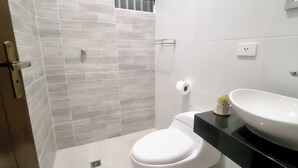 Et badeværelse med et hvidt toilet, en sort vask og et bruseområde med grå fliser.
