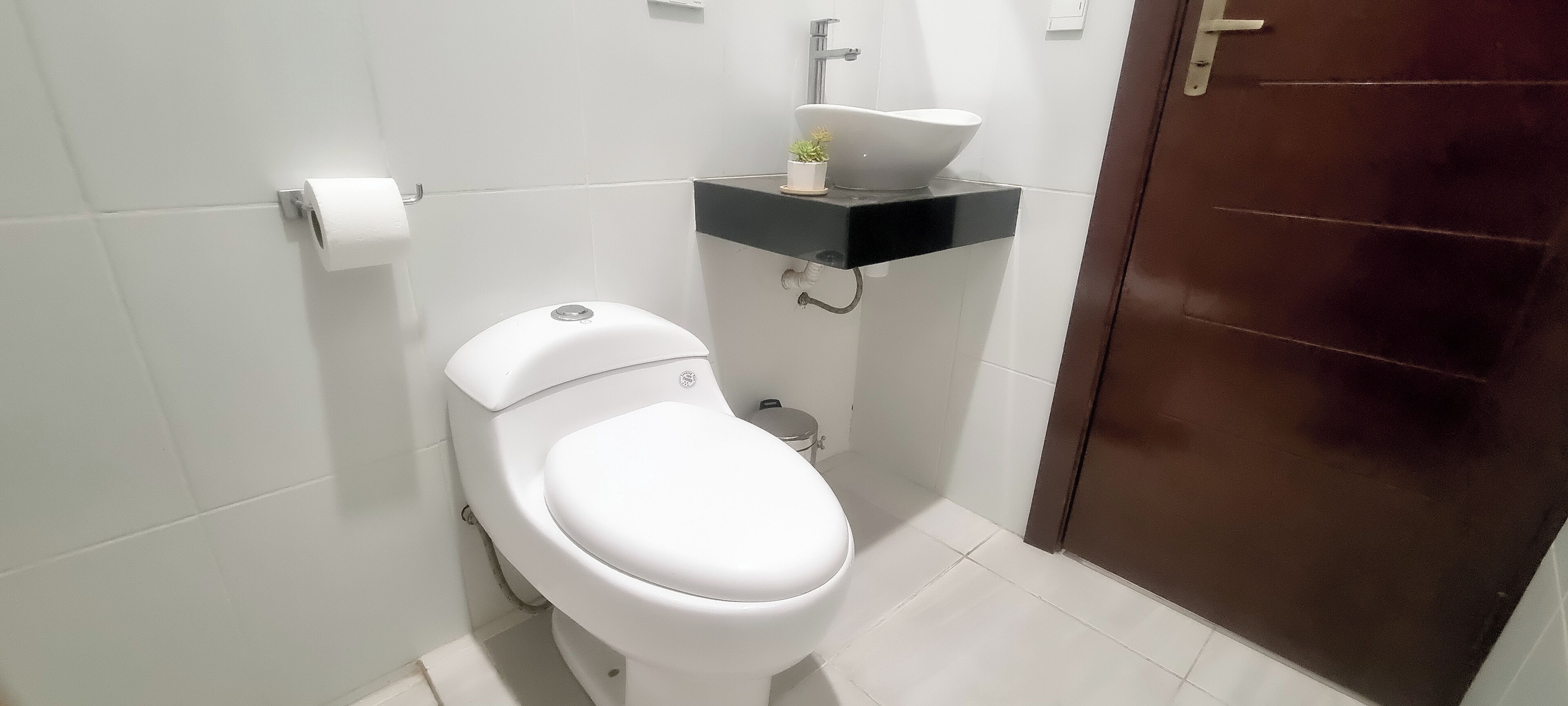 Ein modernes Badezimmer mit einer weißen Toilette, einem schwarzen Waschbecken mit weißer Spüle und einem kleinen Topfpflanzen auf dem Waschbecken.