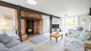 A cozy living room with a brick fireplace, a sofa, a coffee table, and a television. - Hollybank Cottage, Ufford (Ufford)