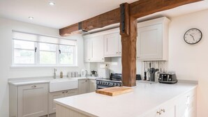 A modern kitchen with white cabinetry, a central island, a stove, and a clock on the wall. - Hollybank Cottage, Ufford (Ufford)