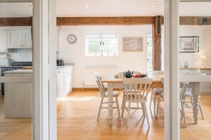 Eine helle Küche mit weißen Schränken, einer Holzbalkendecke und einem Essbereich mit Tisch und Stühlen.