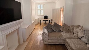 Un salon doté d’un grand téléviseur à écran plat, d’un canapé beige agrémenté de coussins, d’une cheminée blanche et d’un plancher en bois.