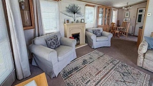 A spacious living room with a fireplace, two sofas, a dining area, and a large window with blinds. - Super 2 bed 6 berth caravan pets go free (Hunstanton)