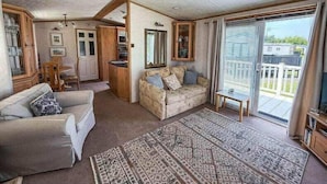A cozy living room with a sofa, a patterned rug, and a dining area with wooden furniture. - Super 2 bed 6 berth caravan pets go free (Hunstanton)