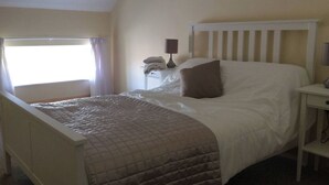 A neatly made bed with a quilted bedspread, a bedside table with a lamp, and a window with curtains.
