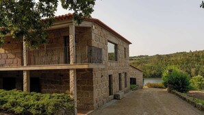 A stone building with a balcony, a paved driveway, and a natural landscape in the background.