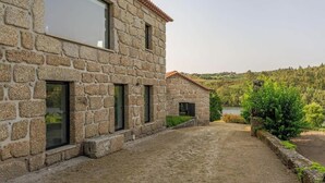 A stone building with a courtyard, a small garden, and a view of a lake and forest.