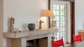 A room with a fireplace, a table with chairs, and a door leading outside. - Quiet Escape by the River w/ Pool by HostWise (Tábua)