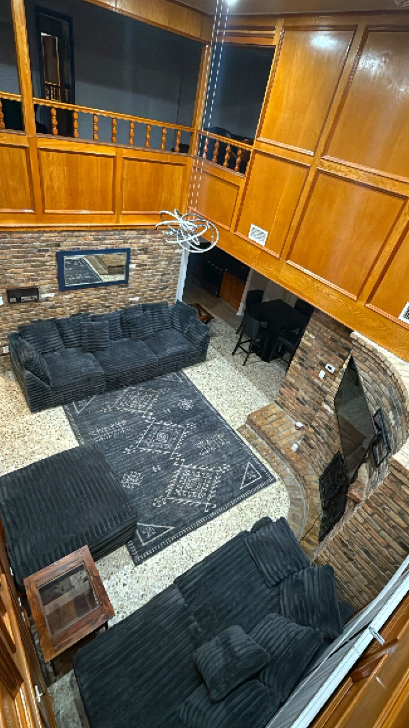 Amplia sala de estar con un sofá modular negro grande, un tapete estampado y una chimenea.