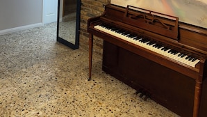 A room with a piano, a large abstract painting, a brick wall, and a door leading to a staircase. - Spacious 5-bedroom house with AC, WiFi in awesome Houston (Houston)