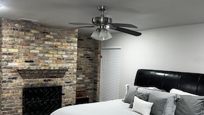A bedroom with a brick fireplace, a ceiling fan, and a bed with striped bedding. - Spacious 5-bedroom house with AC, WiFi in awesome Houston (Houston)