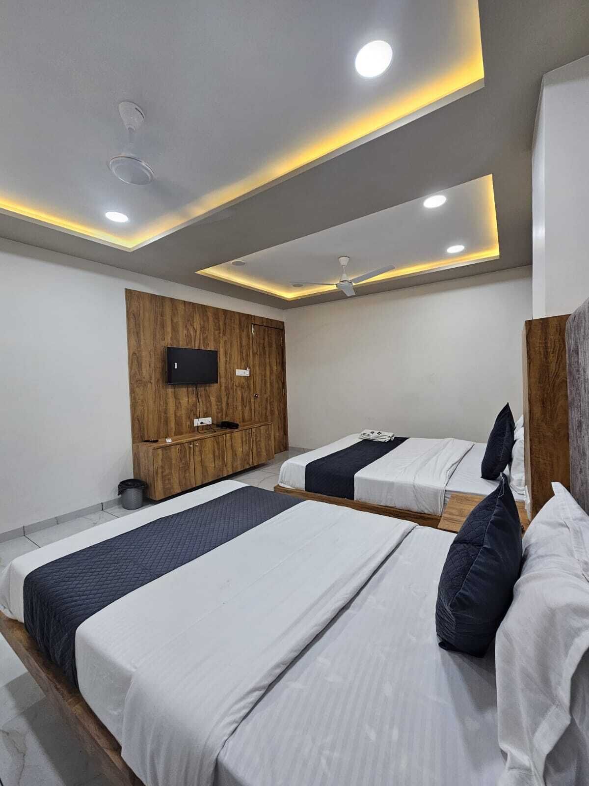 Una habitación de hotel moderna con dos camas, un armario de madera, un televisor de pantalla plana e iluminación empotrada en el techo.