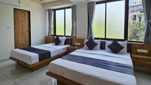 A hotel room with two beds, a ceiling fan, large windows, and a view of the outside. - HOTEL GATEWAY INN (Ahmedabad)