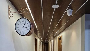A long, well-lit hallway with a hanging wall clock, wooden doors, and a polished floor. - HOTEL GATEWAY INN (Ahmedabad)