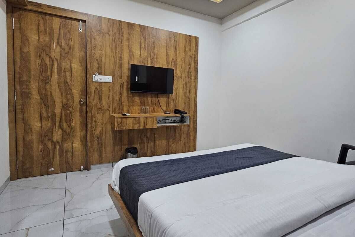 A bedroom with a bed, a TV mounted on a wooden panel wall, a ceiling fan, and recessed lighting.