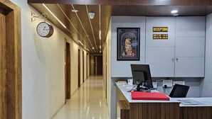 A reception area with a wooden reception desk, a clock, and a reception sign on the wall. - HOTEL GATEWAY INN (Ahmedabad)