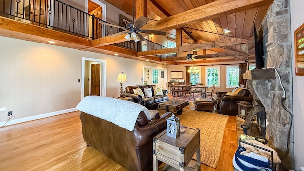 A spacious living room with a high ceiling, wooden beams, a fireplace, and a dining area.
