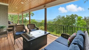 A covered outdoor patio with wicker furniture, a glass-top table, and a view of a mountainous landscape.