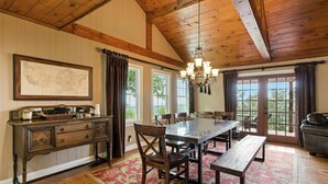 A dining area with a wooden table, chairs, and a bench. There is a chandelier hanging from the ceiling, and a map is displayed on the wall.