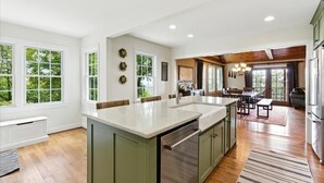 A spacious kitchen with a large island, wooden flooring, and a view of the outdoors through large windows.
