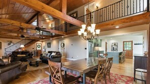A spacious living room with a wooden dining table, leather sofas, and a red patterned rug.
