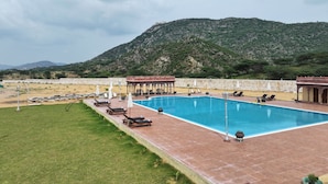 Une piscine entourée d’un mur de pierre et d’une pelouse, avec des chaises longues et des parasols à proximité.