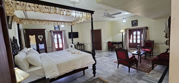 A four-poster bed with a canopy, a desk with a chair, and a red armchair in a room with a tiled floor and a ceiling fan.
