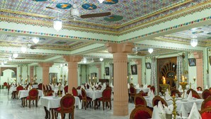 Une vaste salle de banquet dotée d’un plafond richement décoré et de lustres, de nombreuses tables et de chaises recouvertes d’un tissu rouge.