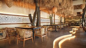 A restaurant with thatched ceiling, patterned walls, and wooden furniture. - Hotel Menaka Inn Dharwad (Dharwad)