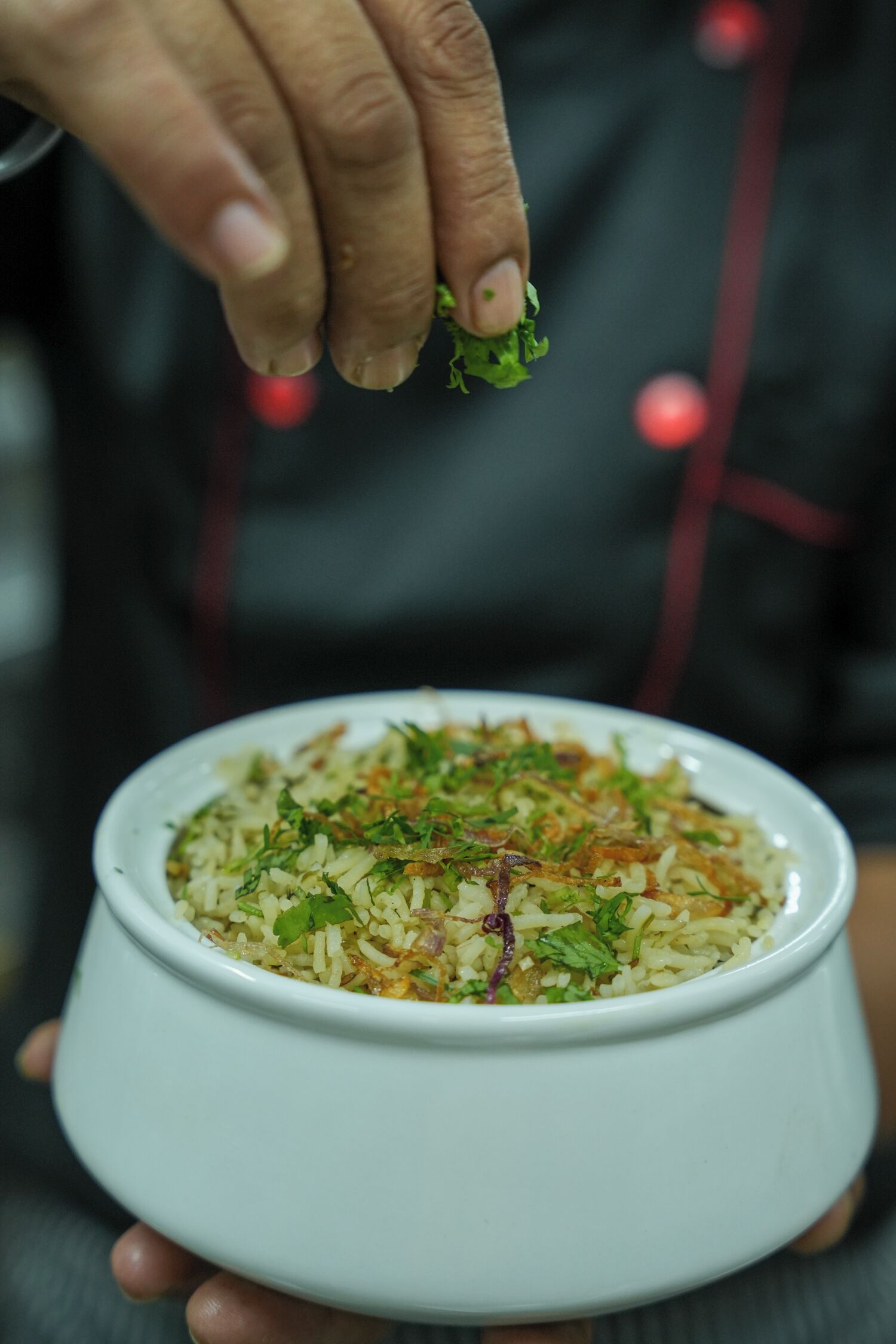 A person holding a bowl of rice with herbs.