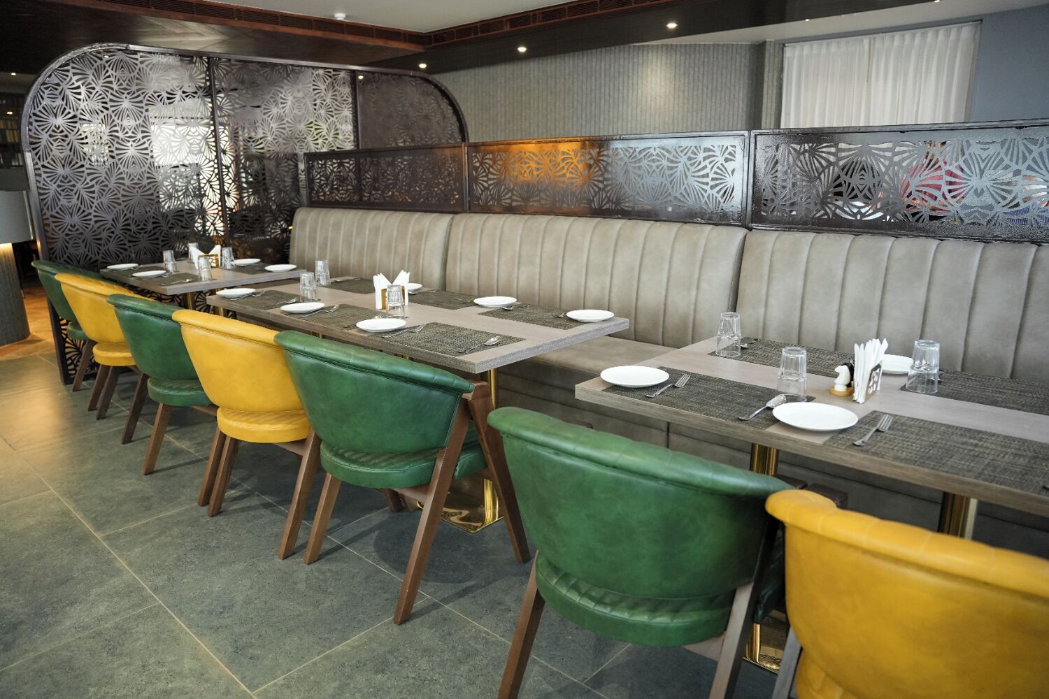 A restaurant with a long counter, green and yellow chairs, and a cushioned bench.