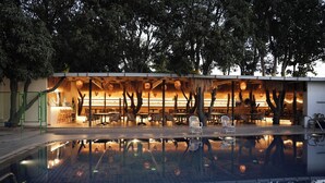 An outdoor pool area with a dining setup under trees, surrounded by a fence. - Hotel Menaka Inn Dharwad (Dharwad)