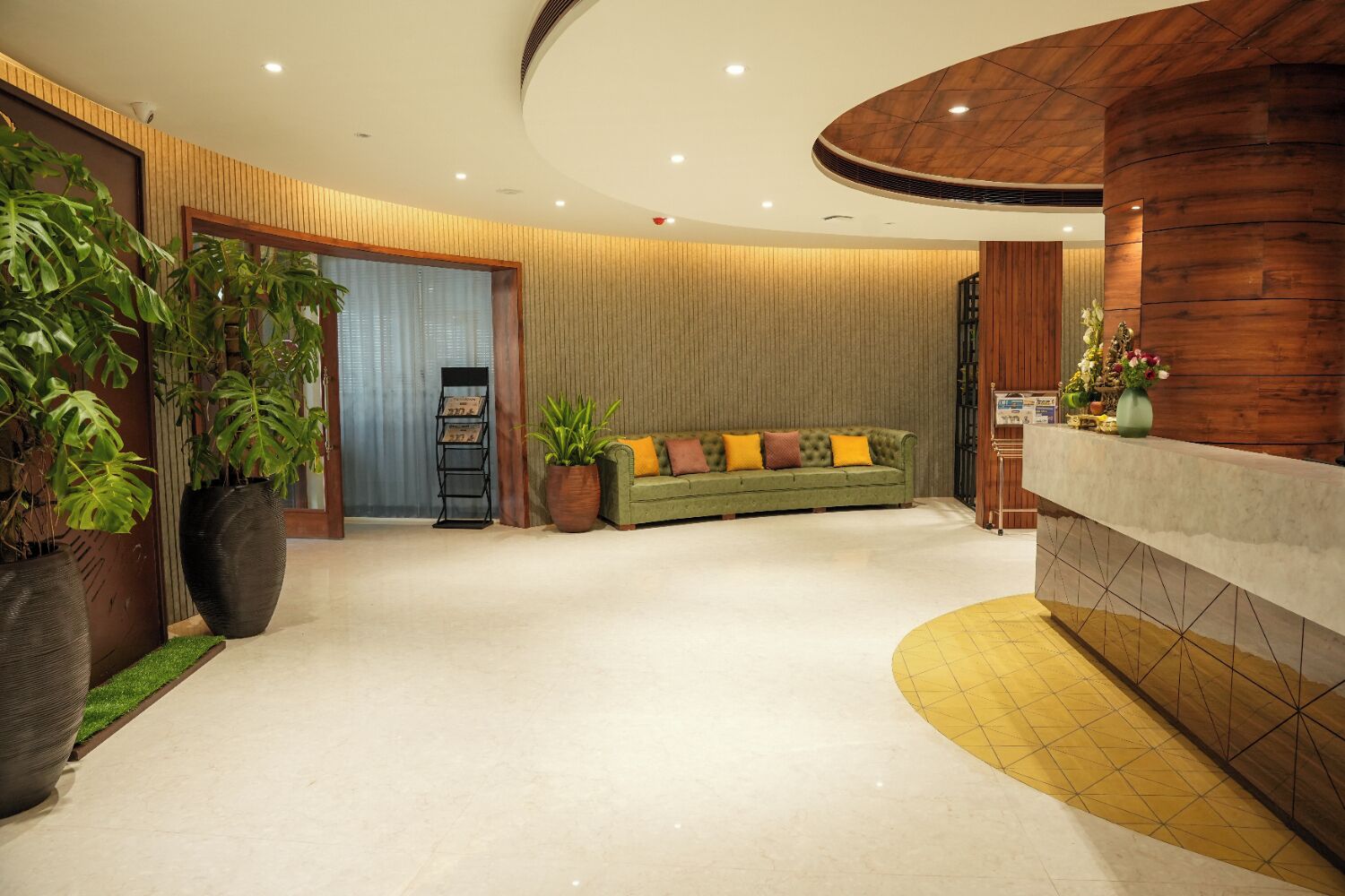 Un área de recepción moderna con un sofá verde, plantas en macetas y un mostrador de madera.