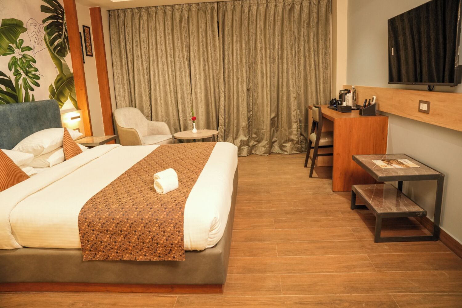 A hotel room with a bed, a desk, a chair, a small table, and a television.