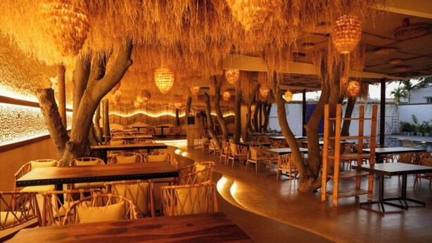 An indoor restaurant with wooden tables and chairs, hanging light fixtures, and a curved seating area. - Hotel Menaka Inn Dharwad (Dharwad)