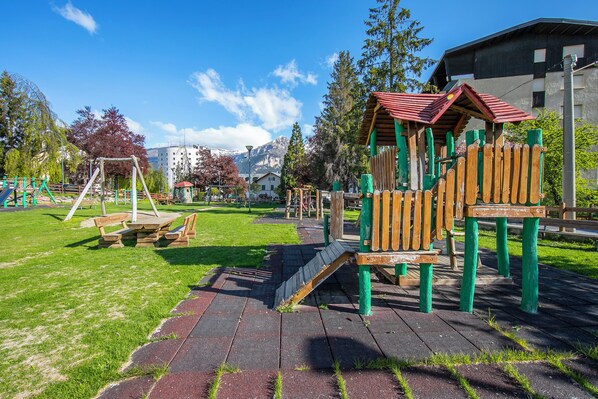 A playground with a wooden play structure, a picnic table, and a paved area.