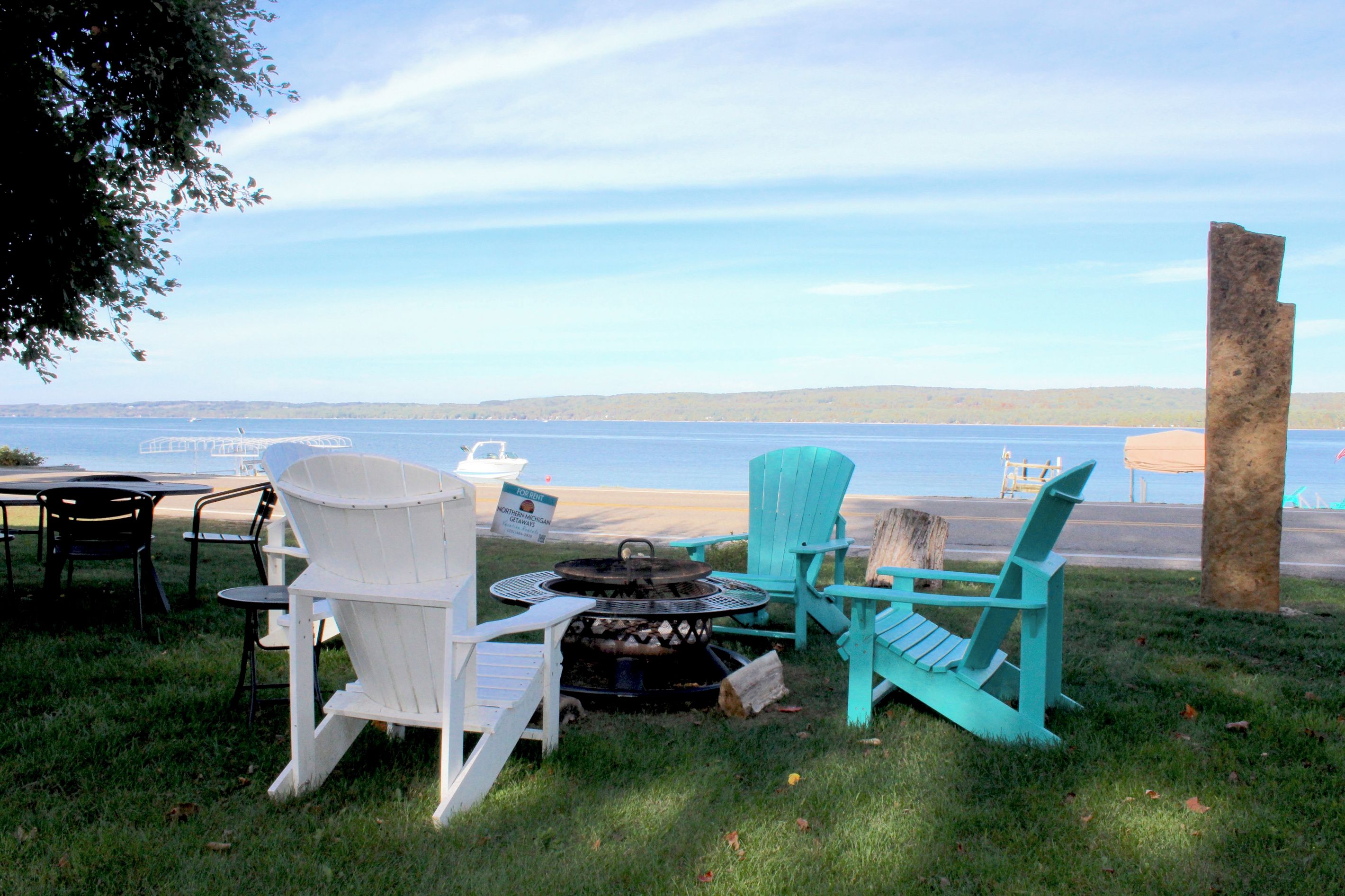 Un espacio de estar junto al lago con sillas Adirondack y una mesa, con vista a una extensión de agua.