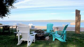 Un espacio de estar junto al lago con sillas Adirondack y una mesa, con vista a una extensión de agua.