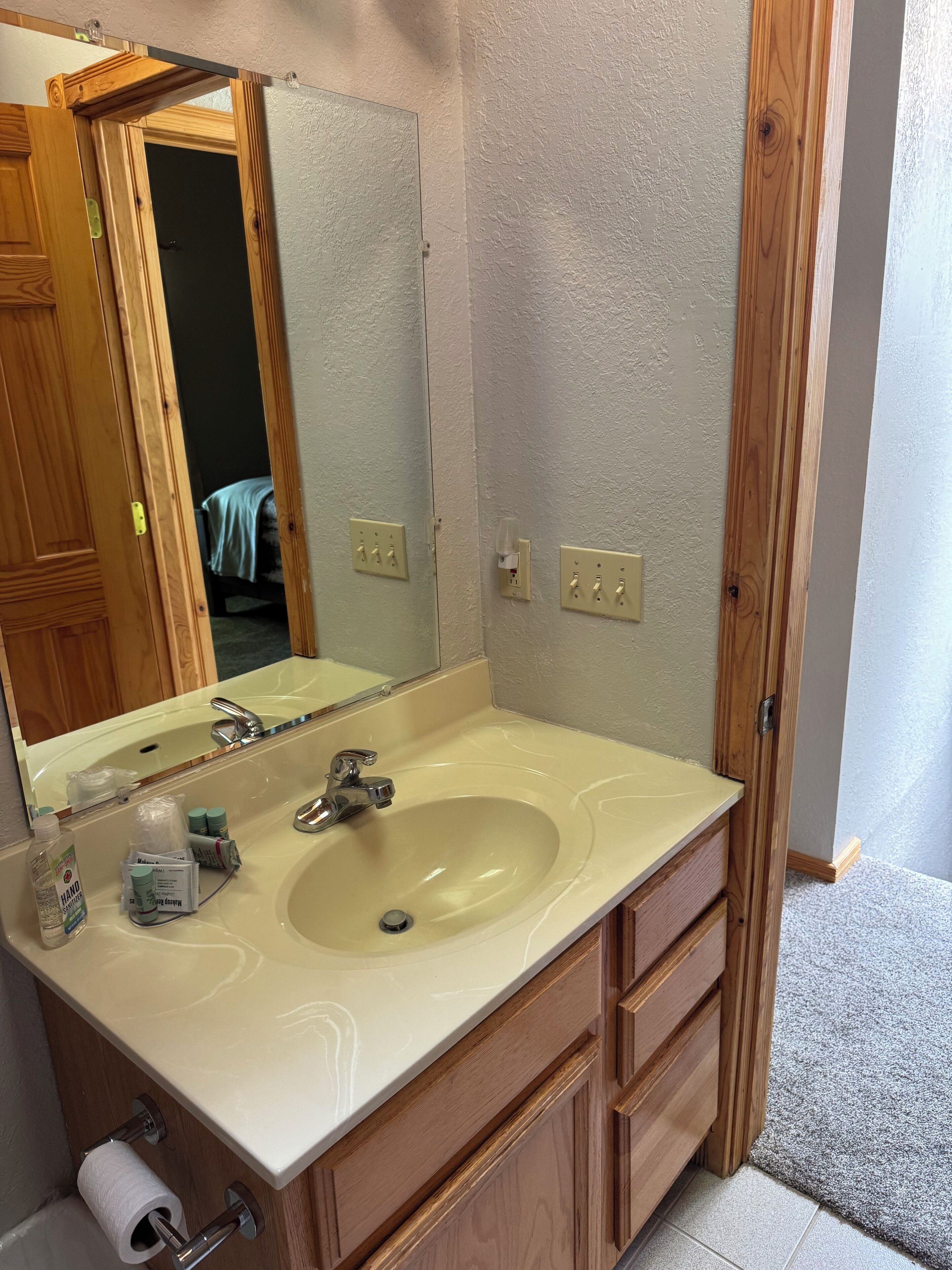 Un bagno con un lavandino color beige, uno specchio e mobili in legno.