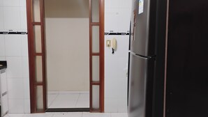 A kitchen with a refrigerator, a door, and a tiled floor.