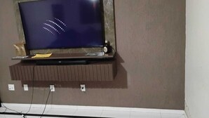 A television mounted on a wall with a brown shelf below it.