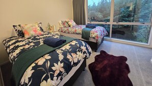 A bedroom with two beds, a large window, and a view of trees.