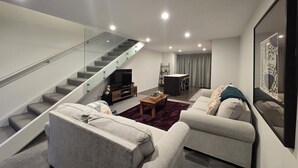 A modern living room with a staircase, a flat-screen TV, and a dining area.