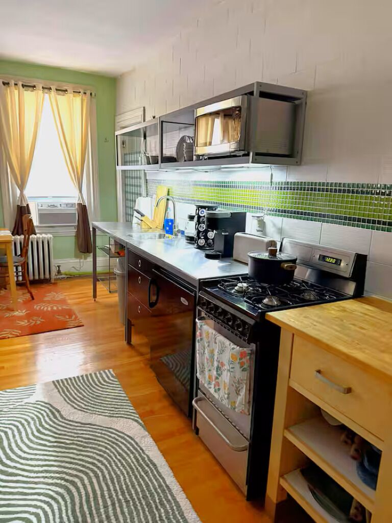 A kitchen with a stove, oven, and microwave, a radiator, and a window with curtains.