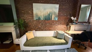 A living room with a brick wall, a sofa, a fireplace, a TV, and a painting.
