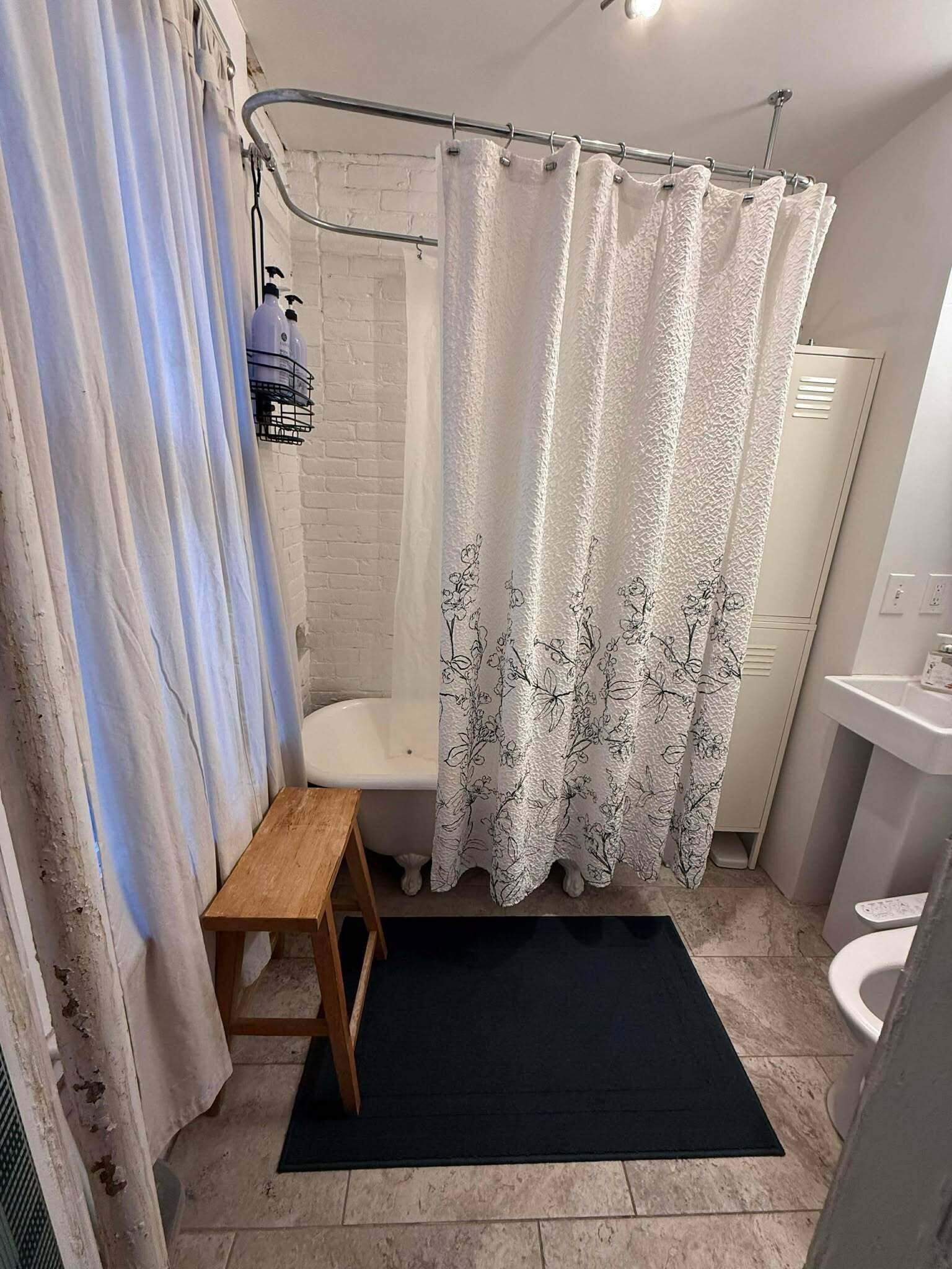 Une salle de bain avec un rideau de douche, un tabouret en bois, un lavabo blanc et des toilettes blanches.