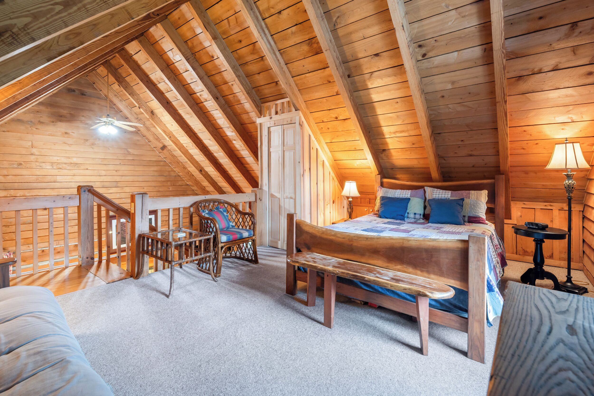 A cozy attic bedroom with a wooden ceiling, a bed with pillows, a chair, and a lamp.