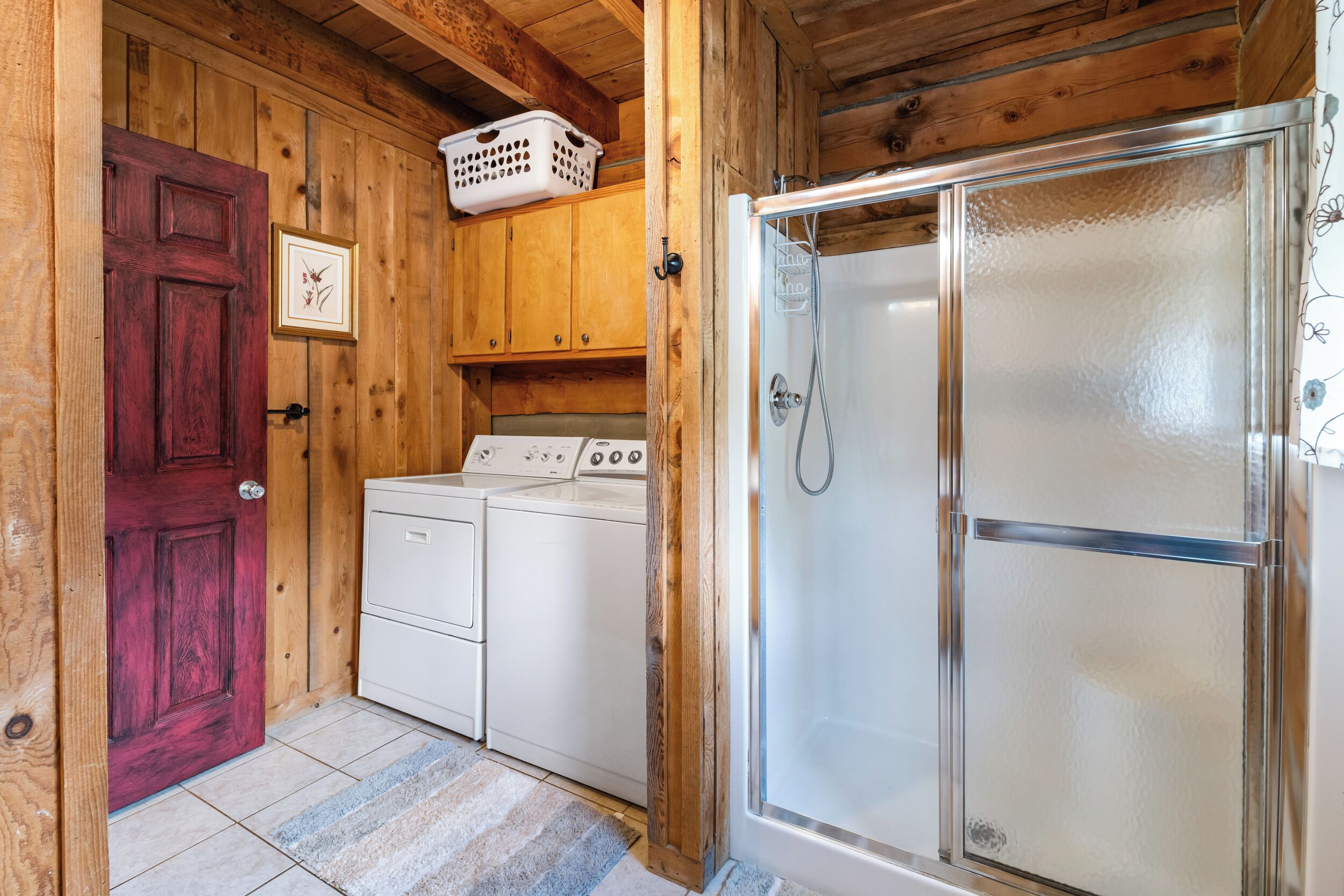Un espace buanderie avec une porte rouge, un lave-linge blanc et une douche fermée par une paroi de verre.