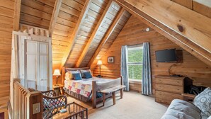 Un dormitorio acogedor con techo de madera, una cama con colcha, un banco, un aparador y un televisor en la pared.