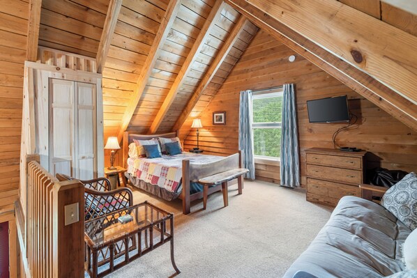 Un dormitorio acogedor con techo de madera, una cama con colcha, un banco, un aparador y un televisor en la pared.